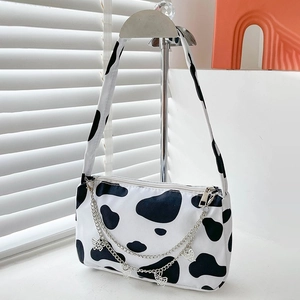 Close-up of cow print canvas bag featuring silver chains and butterfly pendants detail