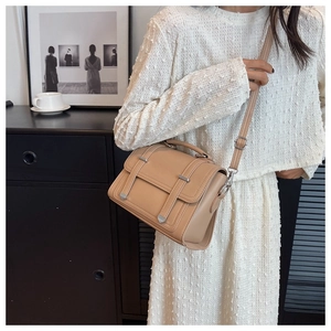 Detail of a minimalist khaki leather crossbody bag with metal buckles and adjustable strap