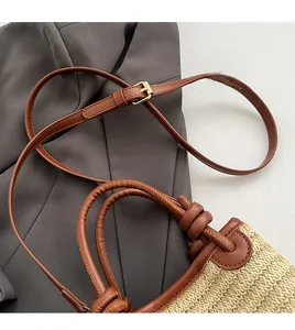 Detail of woven straw bag showing adjustable brown leather strap and wrapped handle