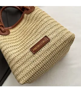 Detail of hand-woven straw tote bag with brown leather handles and logo patch