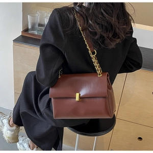 Detail of a brown leather shoulder bag with a gold metal lock and chain strap on a model