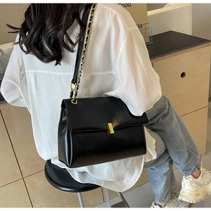 Side view of matte black leather chain tote bag with gold buckle on female model