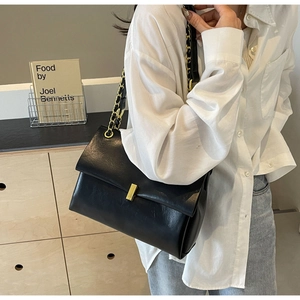 Close-up of black leather tote with golden square buckle and chain strap on shoulder
