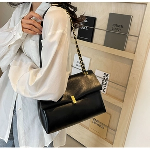 Detail of a black textured leather bag with a gold clasp and woven chain shoulder strap