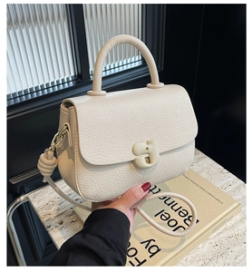Gros plan du sac selle en cuir crème avec texture grainée et boucle artistique en G