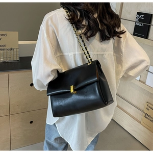 Model wearing a black chain shoulder bag with gold hardware and a flap closure