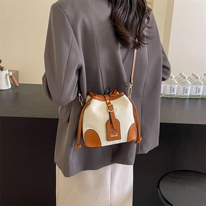 Modische Eimertasche in Creme und Braun auf Modell in grauem Blazer im modernen Design