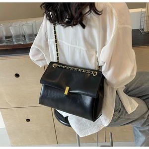 Detail of black faux leather shoulder bag with gold metal clasp and chain strap