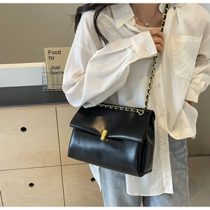 Detail view of black faux leather flap bag with gold chain strap and metal clasp closure