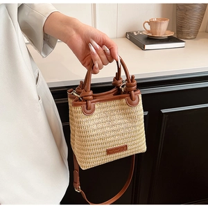 Detail of hand-woven straw bucket bag with dark brown leather trim and knotted handle