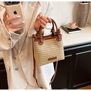 Detail of woven straw bucket bag featuring brown leather trim and shoulder strap