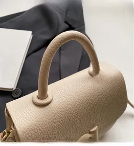 Gros plan sur la poignée en cuir beige grainé et la finition premium du sac besace