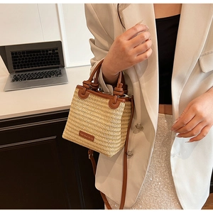 Detail of beige woven straw tote with brown leather handles and brand patch
