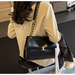 Detail of black textured leather tote with gold buckle and chain strap on a shoulder