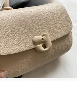 Détail du cuir grainé et de la boucle mate en forme de lettre sur le sac crème