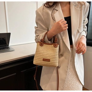 Detail of hand-woven straw bag with premium brown leather trim and chic logo patch