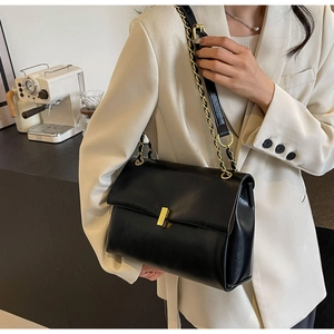 Detail of black leather flap bag with gold rectangular lock and chain shoulder strap