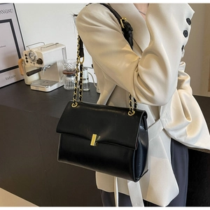 Close-up of black glossy leather handbag with gold metal clasp and chain strap detail
