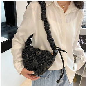 Detail of black quilted shoulder bag featuring glossy finish and pleated strap design