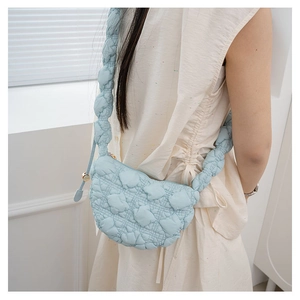 Close-up of light blue quilted dumpling bag with thick padded strap on model