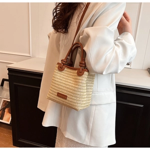 Detail of hand-woven straw bucket bag with brown leather straps styled on white outfit