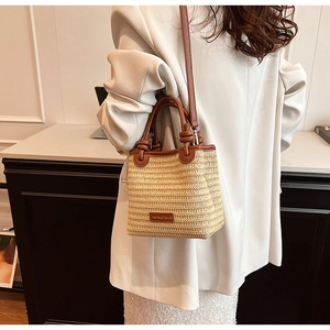 Straw tote bag with brown leather handles worn by a model in a white blazer suit