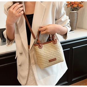 Detail of hand-woven straw bag with dark brown leather handle and brand patch