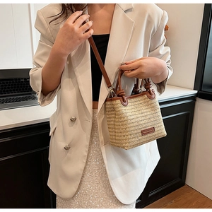 Close-up of beige straw woven bag with brown leather handles and brand logo tag