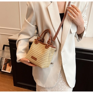 Detail of hand-woven straw tote with brown leather trim and adjustable shoulder strap