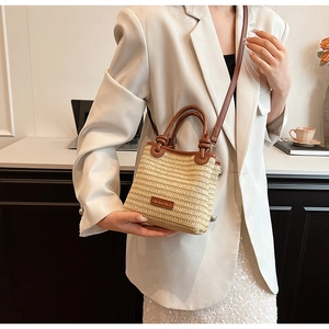 Detail of beige straw bucket bag with brown leather trim and knotted shoulder strap