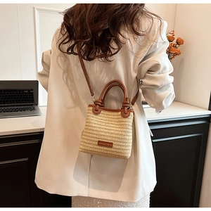Detail of small straw bucket bag with brown leather handles and brand logo tag