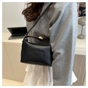 Detail of black pleated crossbody bag with gold hardware worn by a model in a modern office