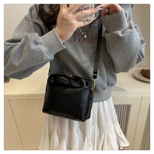 Close-up of black pleated crossbody bag with gold buckle on casual model look