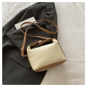 Detail of a two-tone crossbody bag with pleated fabric and brown leather strap on a blazer