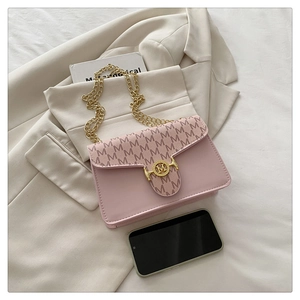 Detail of pink crossbody bag with brown monogram flap and gold chain strap on beige suit