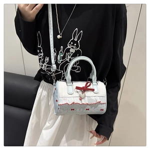 Detail of blue cylinder bag with red bows, lace trim, and silver heart pendant