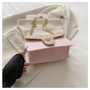 Detail of pink crossbody bag with gold chain strap and M-pattern texture on beige suit