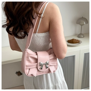 Close-up of a pink pleated shoulder bag featuring a silver butterfly buckle in a chic setting