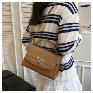 Close-up of brown handbag featuring woven texture flap and golden hardware accents