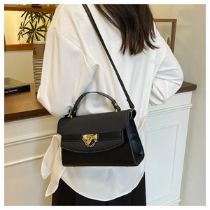 Classic black handbag with gold chain detail shown on a model in a cozy cafe setting