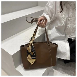 Detail of dark brown leather tote bag with white stitching and stylish silk scarf handle