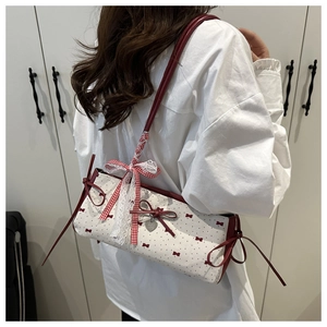 Detailed side view of the cream shoulder bag with red bows and lace ribbon accents