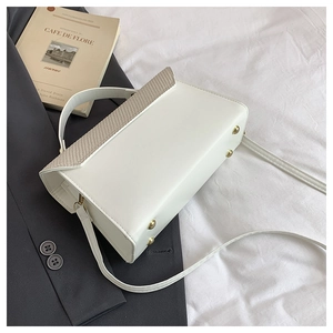 Detail of white PU leather handbag with woven flap and protective gold feet studs