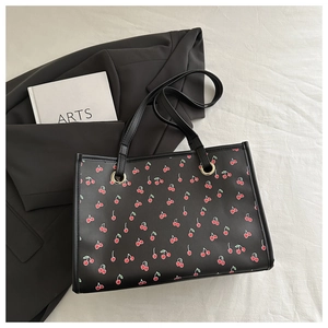 Close-up of a floral tote bag with cherry print and metallic eyelets on white fabric