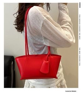 Close-up of red leather tote bag with side pendant shown on model in white outfit