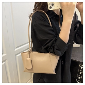 Gros plan d'un sac à bandoulière trapèze beige minimaliste avec surpiqûres et pendentif