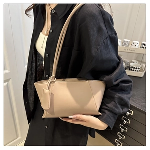 Detail of minimalist beige trapezoid leather handbag with slim straps and chic charm accessory