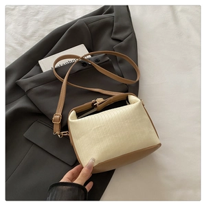 Detail of beige pleated fabric crossbody bag with brown leather accents and gold hardware