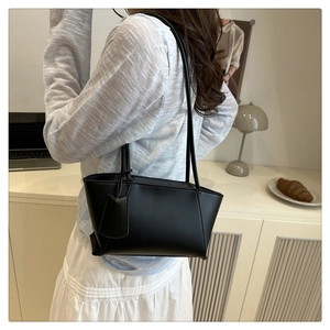 Minimalist black leather baguette bag worn over the shoulder with a trapezoid shape
