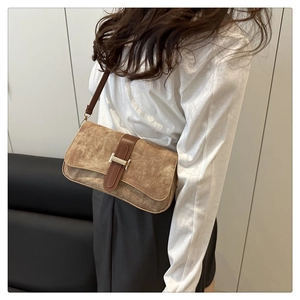 Détail du sac baguette en daim marron avec boucle en métal argenté en forme de H et sangle